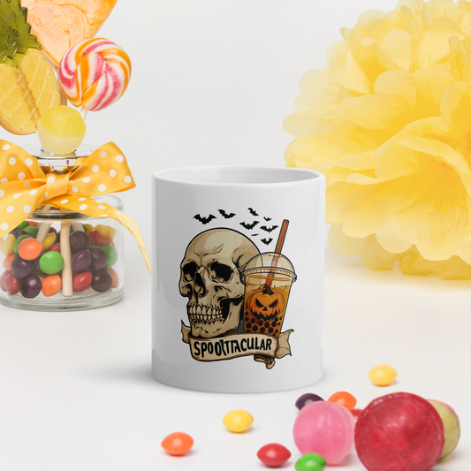 White mug with skull design and 'Spooktacular' text, surrounded by Halloween-themed candies and decorations.