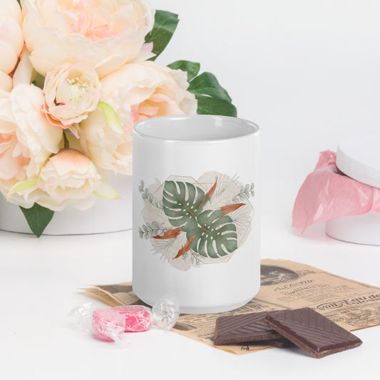 White mug with floral design on a table with flowers, chocolate, and candies.