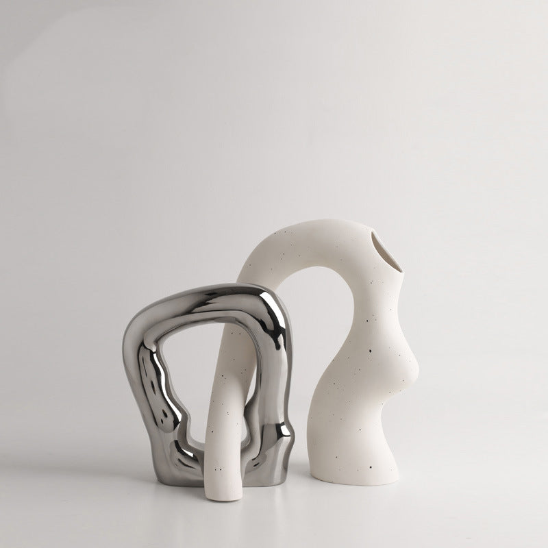 Two ceramic sculptures, one silver and one white, on a light gray background