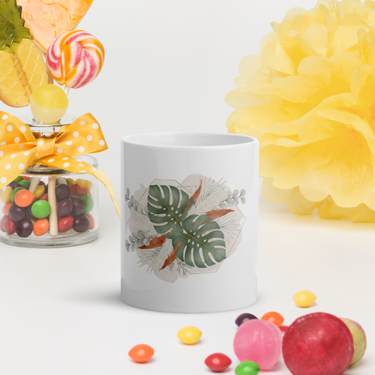 White mug with leaf design surrounded by colorful candies and a yellow flower on a white background